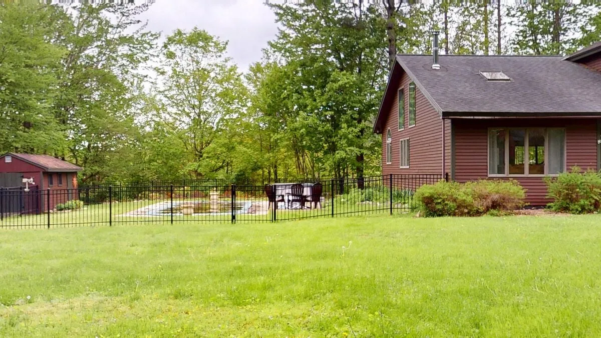 A tranquil view of the house with a fenced yard, outdoor seating area, and visible pool. The setup hints at opportunities for barbecues, quiet relaxation, and family fun in a secure and scenic space.