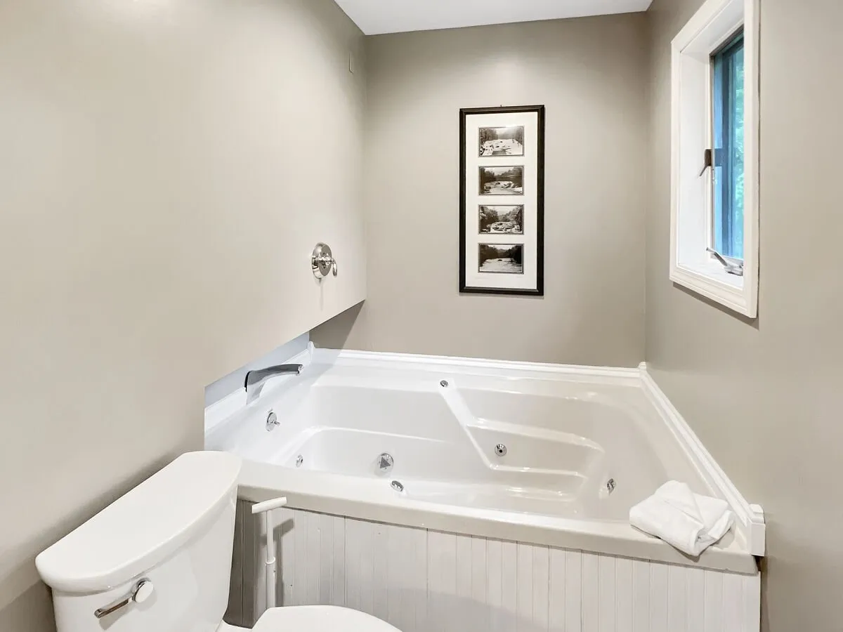 This bathroom features a jacuzzi tub, framed photographs, and a window letting in natural light. The atmosphere is tranquil and spa-like, perfect for a luxurious soak after a busy day.