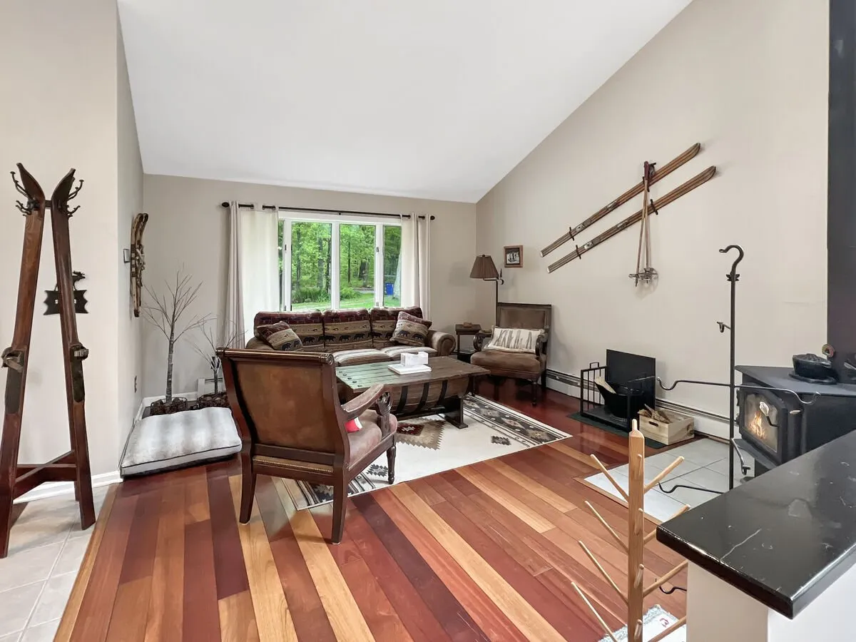 A warm, inviting living area featuring a plush sofa, roaring fireplace, large windows with views to the outdoors, and decorative vintage skis. The scene evokes cozy evenings spent unwinding by the fire after invigorating days exploring nearby mountains or lakes.