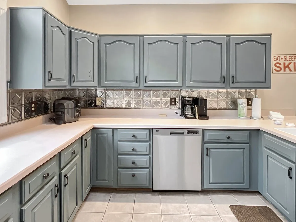 This cozy kitchen scene showcases blue cabinets, a striking silver tile backsplash, and contemporary appliances. The setup hints at celebrations, family gatherings, and recipe sharing around a welcoming kitchen space.
