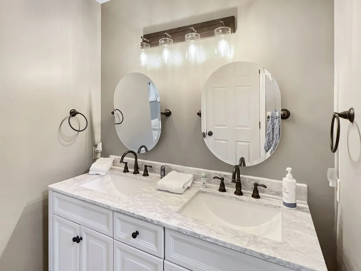 A fresh, inviting bathroom with double sinks, large mirrors, and a bright light fixture—ideal for morning routines and self-care.