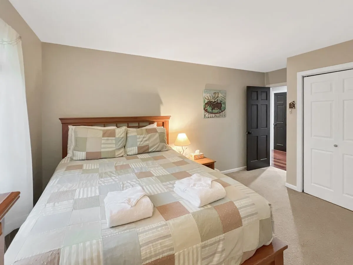 This image shows a bedroom with a patterned quilt on the bed, a nightstand with a lamp, and decorative wall art. The space feels calm and cozy, ideal for resting or reading.