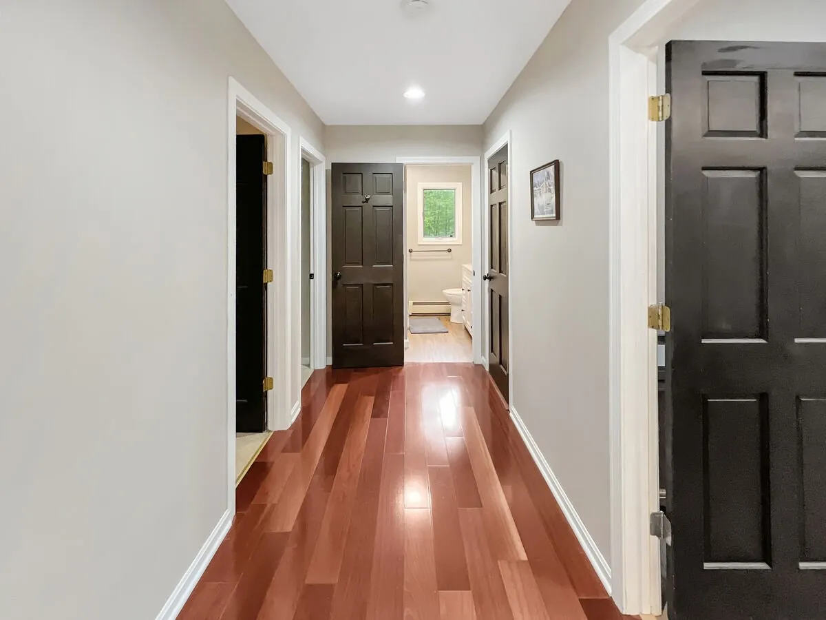 A spacious hallway with richly colored wooden floors and black doors leads guests toward the main living areas. A framed picture on the wall and the clean, open space evoke a sense of transition and invitation, hinting at the broader home beyond and a welcoming return after outdoor adventures.